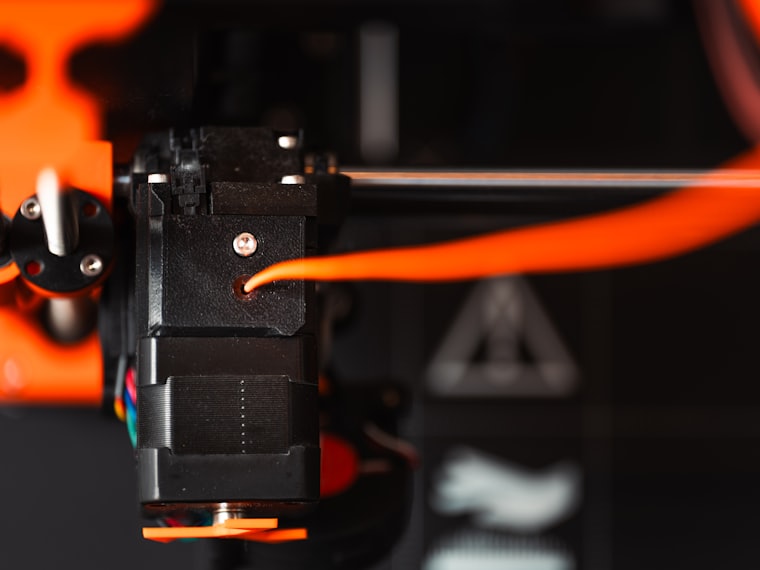 Close-up nozzle 3D printer dengan filamen oranye